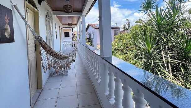 Un balcón techado con una hamaca, paredes blancas y vistas a plantas tropicales.