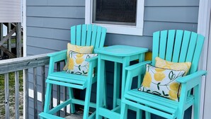 Two turquoise Adirondack chairs with yellow and white patterned cushions on a wooden deck, adjacent to a gray house with a white window. - Newly Renovated Beach Bungalow - 3 minute walk to the beach! (Surf City)