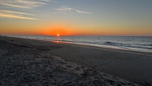 A beach with a sunset over the ocean, sandy shore, and footprints in the sand. - Newly Renovated Beach Bungalow - 3 minute walk to the beach! (Surf City)