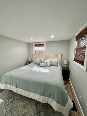 A bedroom with a bed, nightstands, a window with blinds, and a patterned rug.