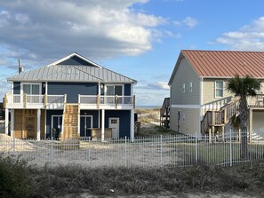 A two-story house with a balcony, a garage, and a sandy beach in the background.