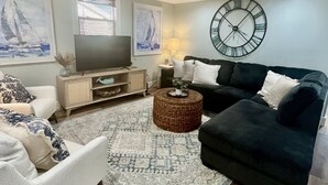 A living room with a sofa, armchair, coffee table, and a TV on a wooden cabinet. - Newly Renovated Beach Bungalow - 3 minute walk to the beach! (Surf City)