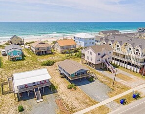 A coastal residential area with houses, some elevated on stilts, and a beach in the background.