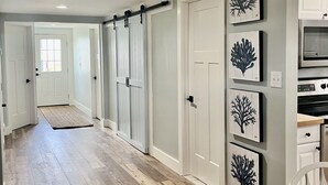 A hallway with wooden flooring, white doors, and wall-mounted artwork. - Newly Renovated Beach Bungalow - 3 minute walk to the beach! (Surf City)
