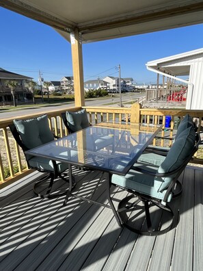 A covered outdoor deck with a glass-top table and four chairs, overlooking a residential area with houses and a road.