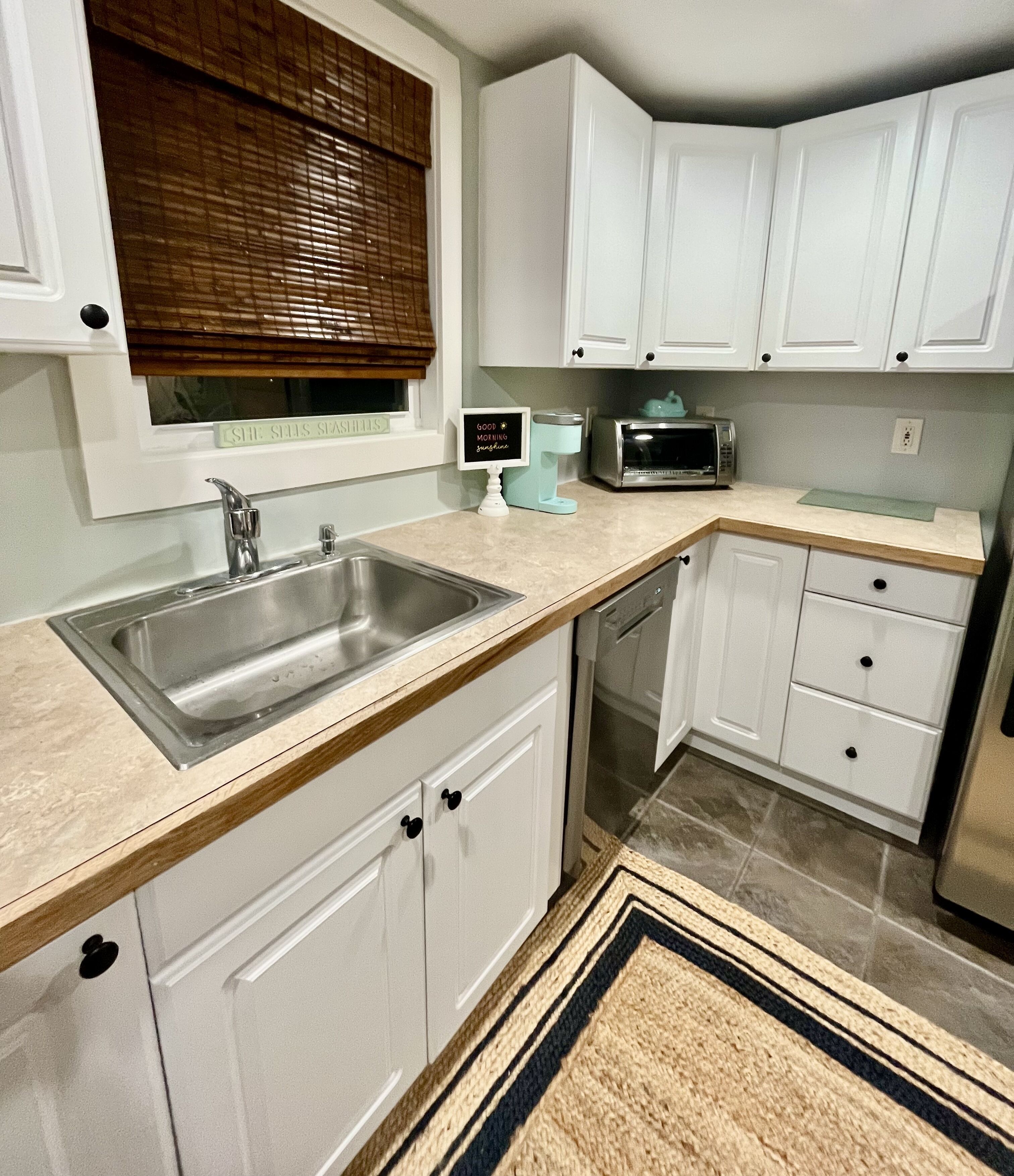A kitchen with white cabinets, a stainless steel sink, a microwave, and a dishwasher.