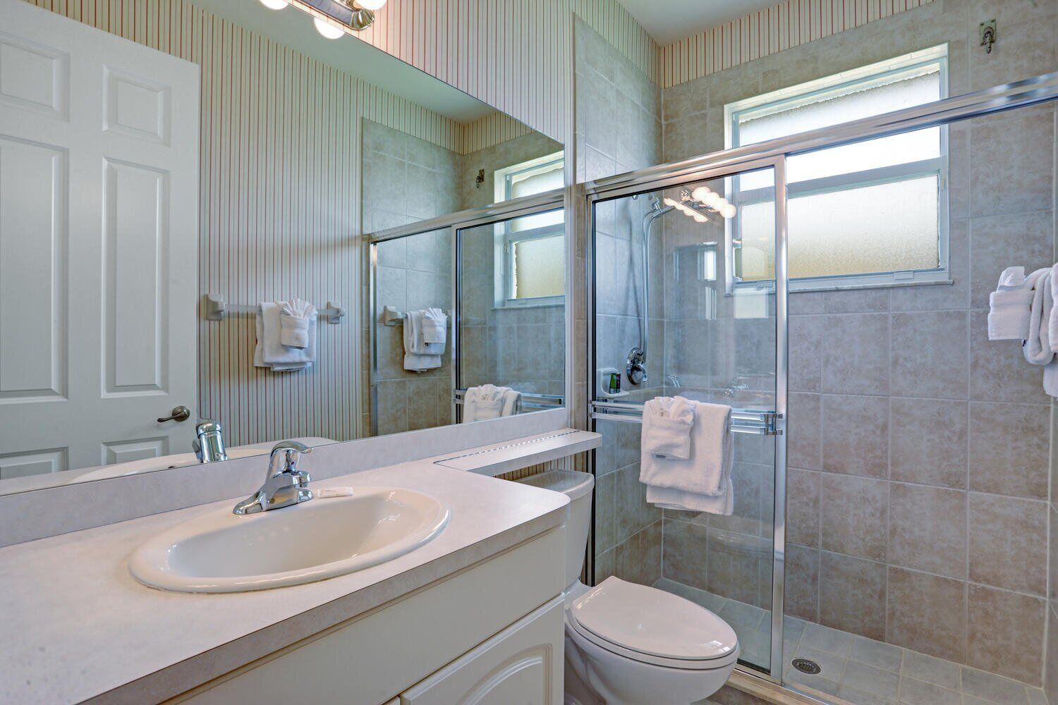 A modern bathroom with a large mirror, a sink, a toilet, and a glass-enclosed shower.