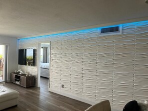 Un salon moderne doté d’un mur à texture originale, d’un téléviseur à écran plat, d’un meuble en bois et d’un canapé.