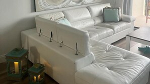 Un salon moderne avec un canapé en cuir blanc, un grand tableau abstrait et deux lanternes turquoise posées sur le sol.