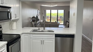 Une cuisine moderne avec des meubles blancs, des appareils en acier inoxydable et une grande fenêtre donnant sur un balcon.
