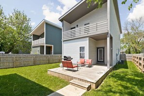 A two-story house with a deck, a barbecue grill, and outdoor seating.