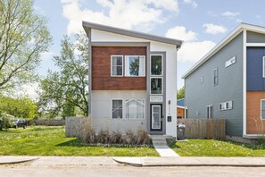 A modern two-story residential building with a flat roof, large windows, and a visible front door.