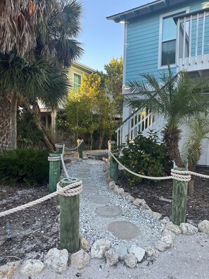 A pathway leading to a building with a blue exterior, surrounded by palm trees and a garden area with a rope barrier.