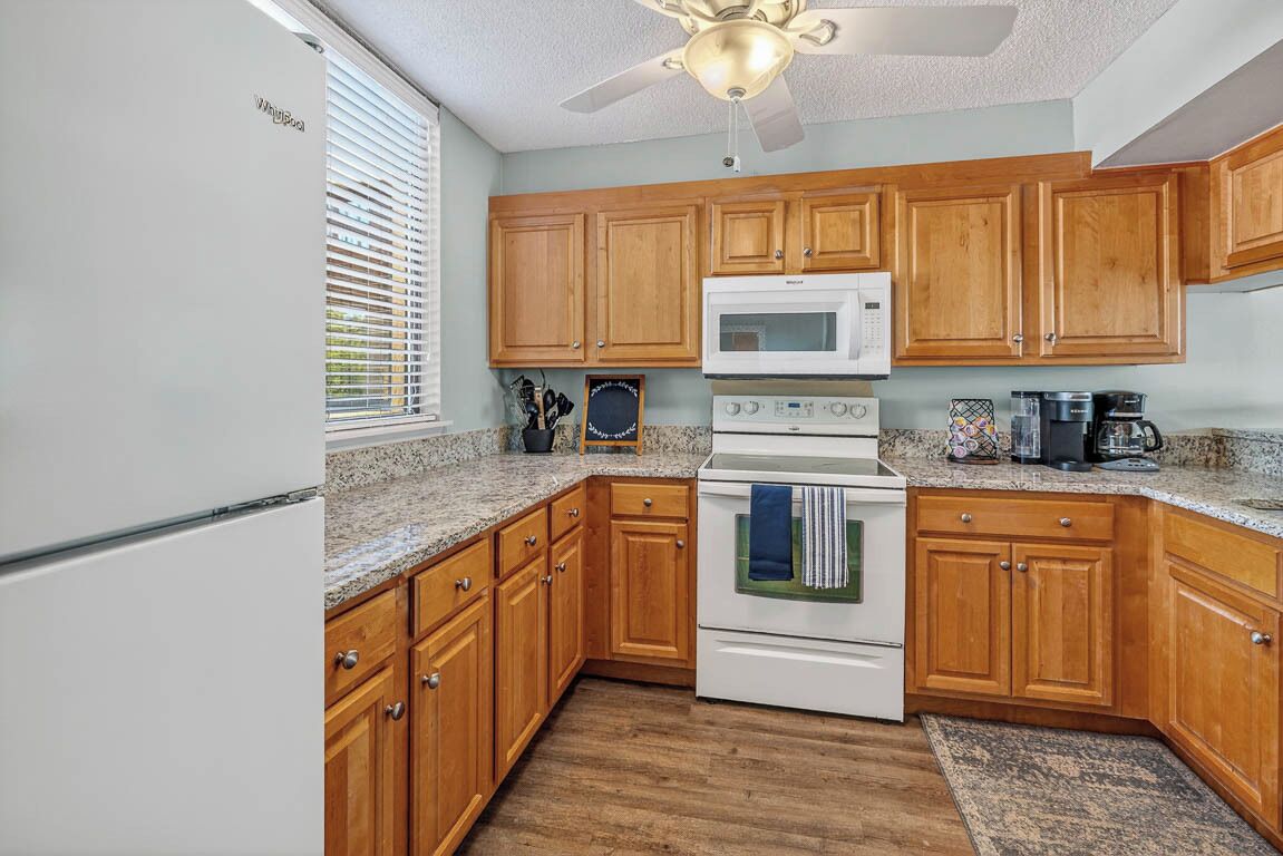 A compact kitchen with wooden cabinets, a white refrigerator, a microwave, a stove, and a ceiling fan.