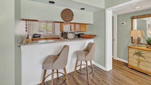 A kitchen with a central island, two bar stools, wooden cabinets, and a decorative mirror.