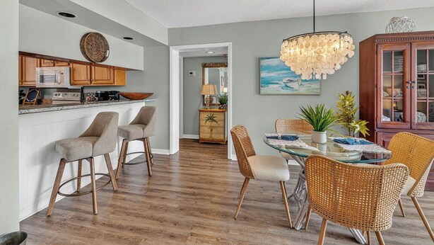 A modern kitchen with a bar area, dining space with wicker chairs, and a wooden cabinet.