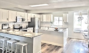 Una cocina moderna con armarios blancos, una isla grande con taburetes de bar, horno empotrado y refrigerador.