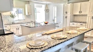 A modern kitchen with white cabinetry, granite countertops, and a central island with stools.