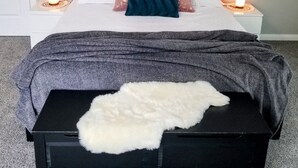 A bedroom with a bed, two bedside tables with lamps, a painting on the wall, and a fur throw on the bed.
