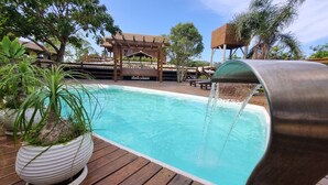A swimming pool with a water feature, surrounded by wooden decking and potted plants. - Arte da Tribo Hsotel & Camping - Hostel (Imbituba)