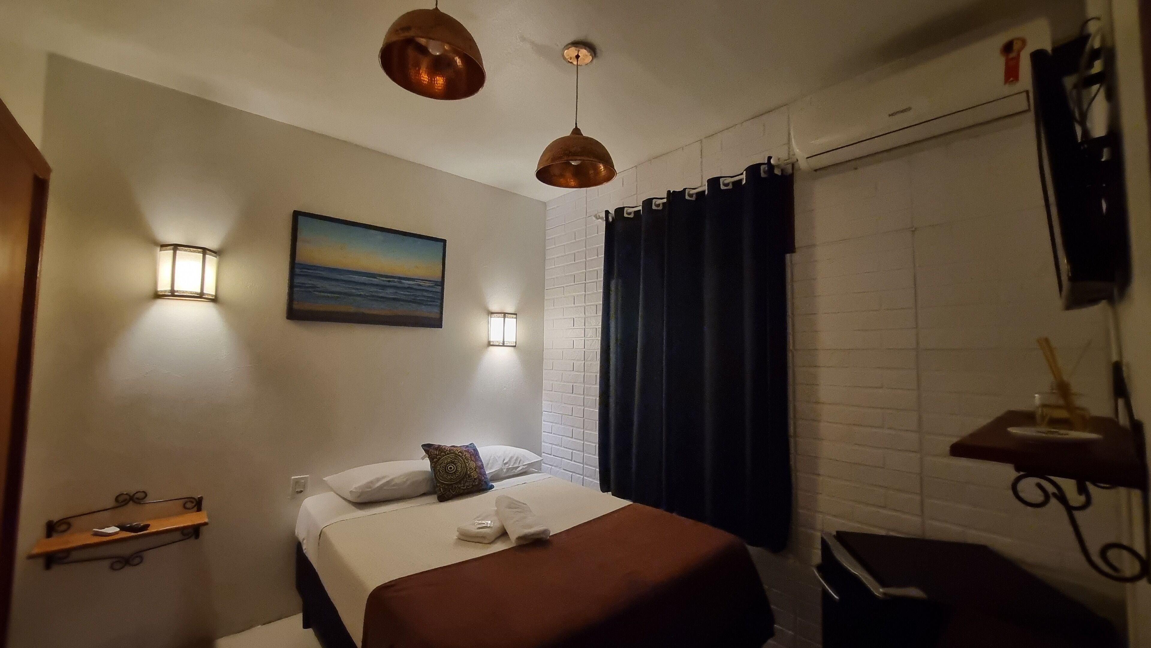 A hotel room with a bed, a painting, a wall-mounted shelf, and a window with curtains.