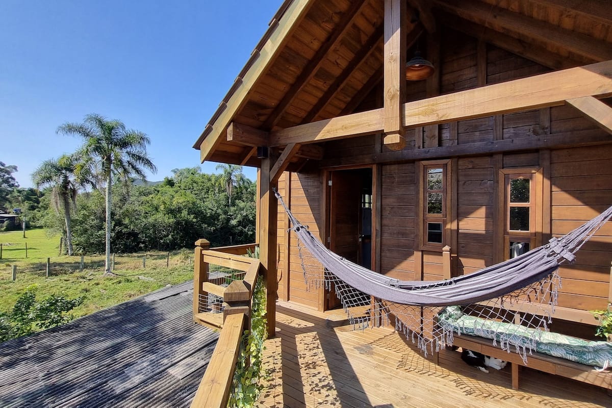 Une cabane en bois avec un hamac sur le porche, une terrasse en bois et une vue sur la verdure environnante.