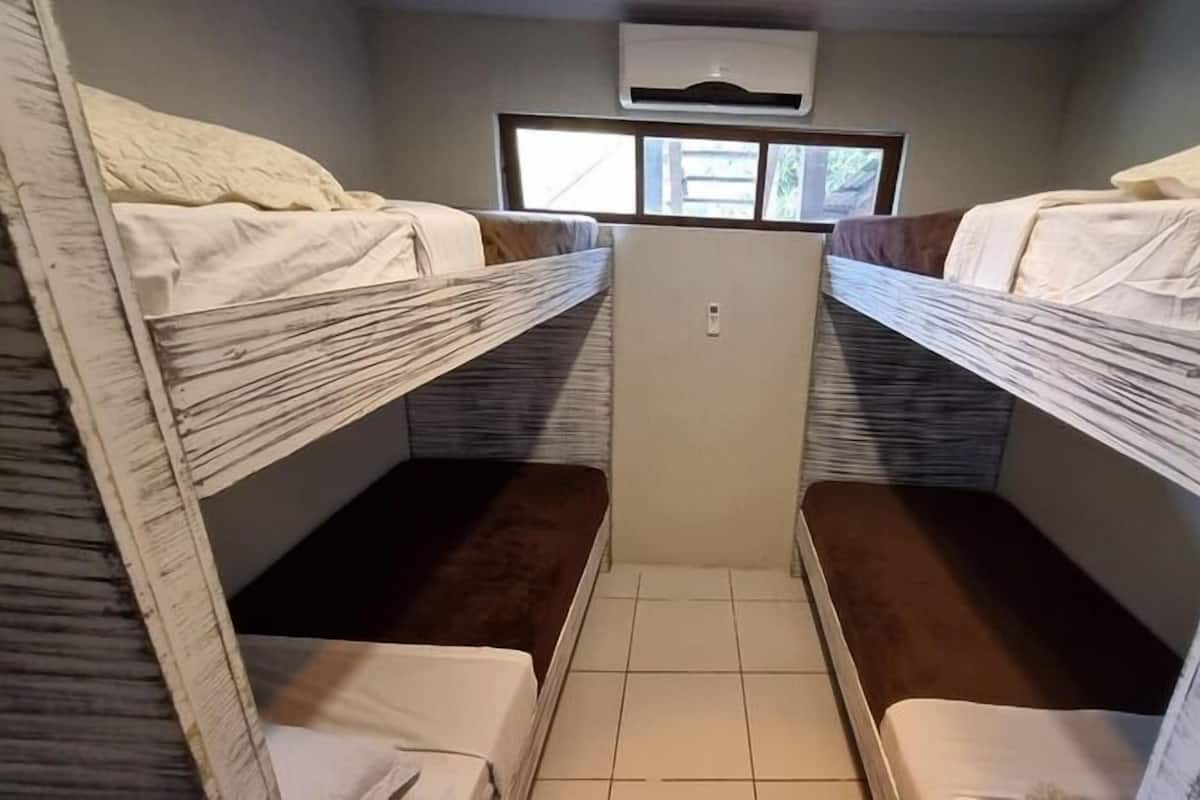 Une petite pièce avec deux lits superposés, une petite fenêtre et un appareil de climatisation central.