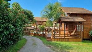 A wooden cabin with a deck, surrounded by lush greenery and a gravel path. - Arte da Tribo Hsotel & Camping - Hostel (Imbituba)
