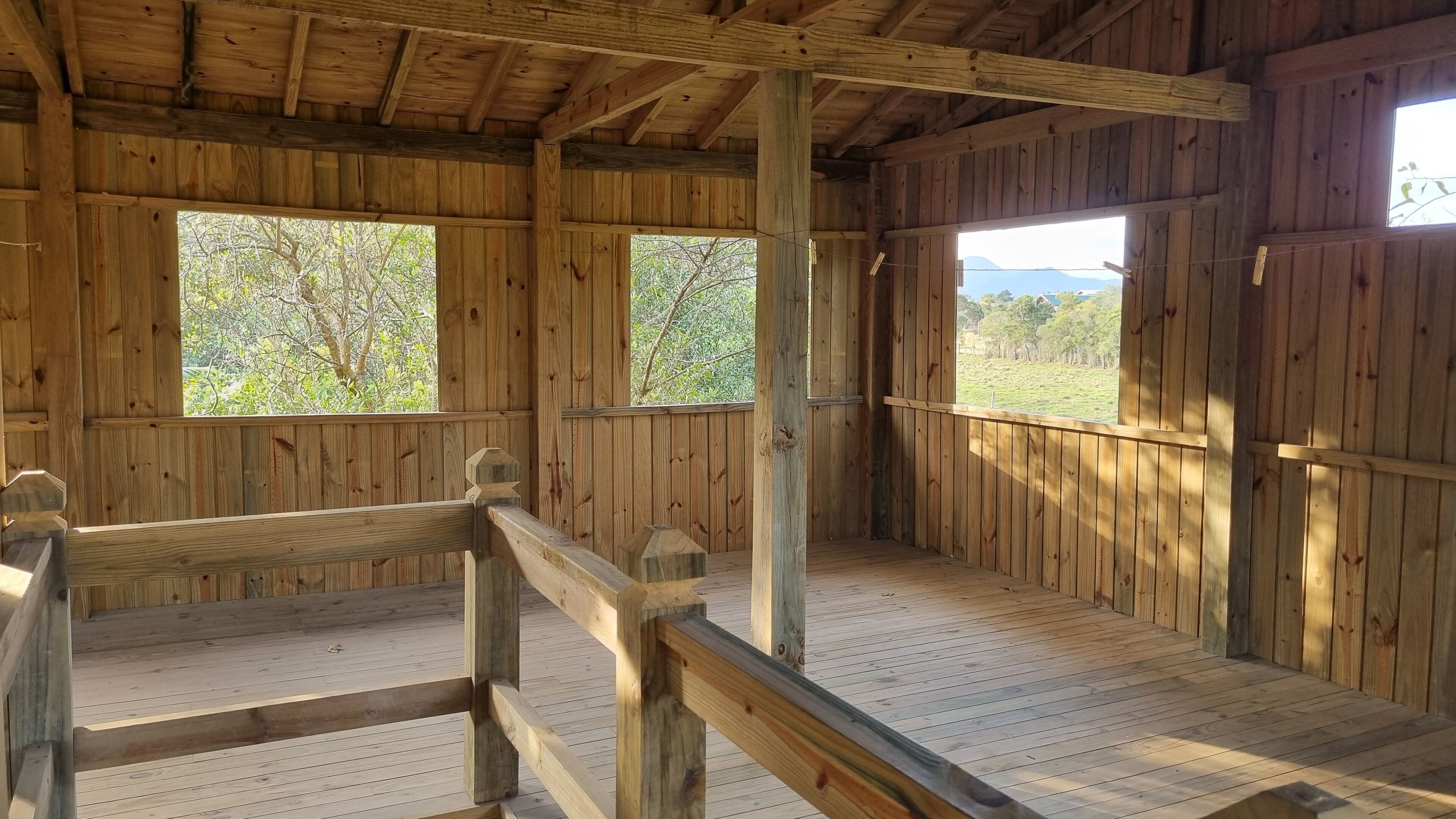 A wooden cabin with a wooden deck, large windows, and a view of the outdoors.