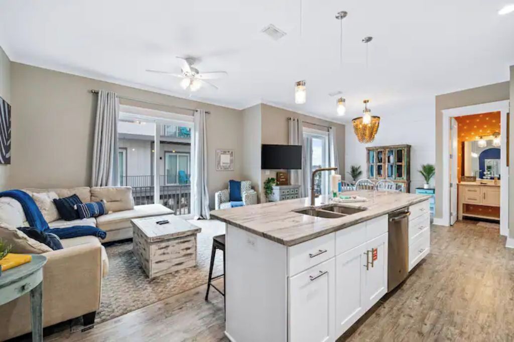 A modern kitchen with a central island, white cabinetry, and a dining area with a sofa and coffee table.