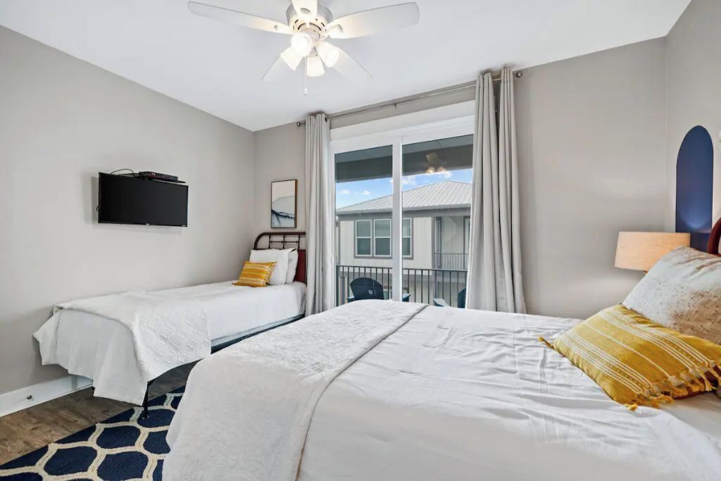 A hotel room with two beds, a ceiling fan, a TV, and a view of the outside.
