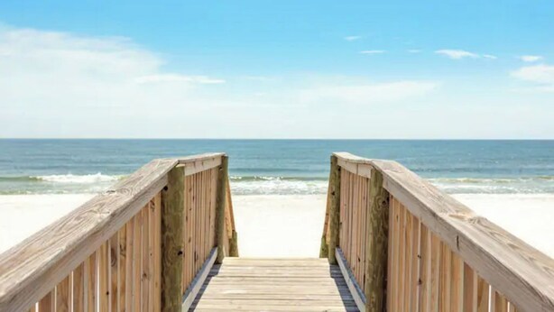 A wooden boardwalk leading to a beach with a clear view of the ocean.