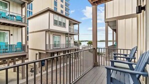 A balcony with a view of the sea, a wooden deck, and a building with multiple floors and balconies.