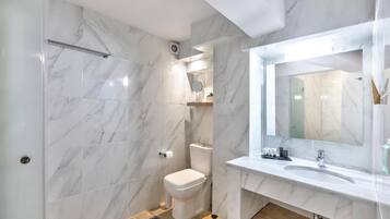 A modern bathroom with marble tiles, a white toilet, a sink with a mirror, and a shower area.