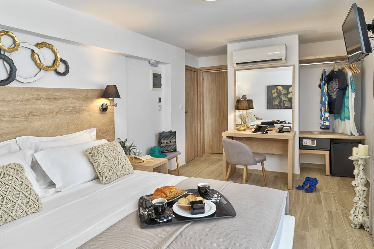 A hotel room with a bed, a desk, and a TV. There is a tray with breakfast on the bed.
