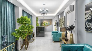 A modern interior with a marble floor, teal sofas, a chandelier, and a staircase leading to a kitchen area. - ACROPOLIS CITY LIFE BH (Athens)