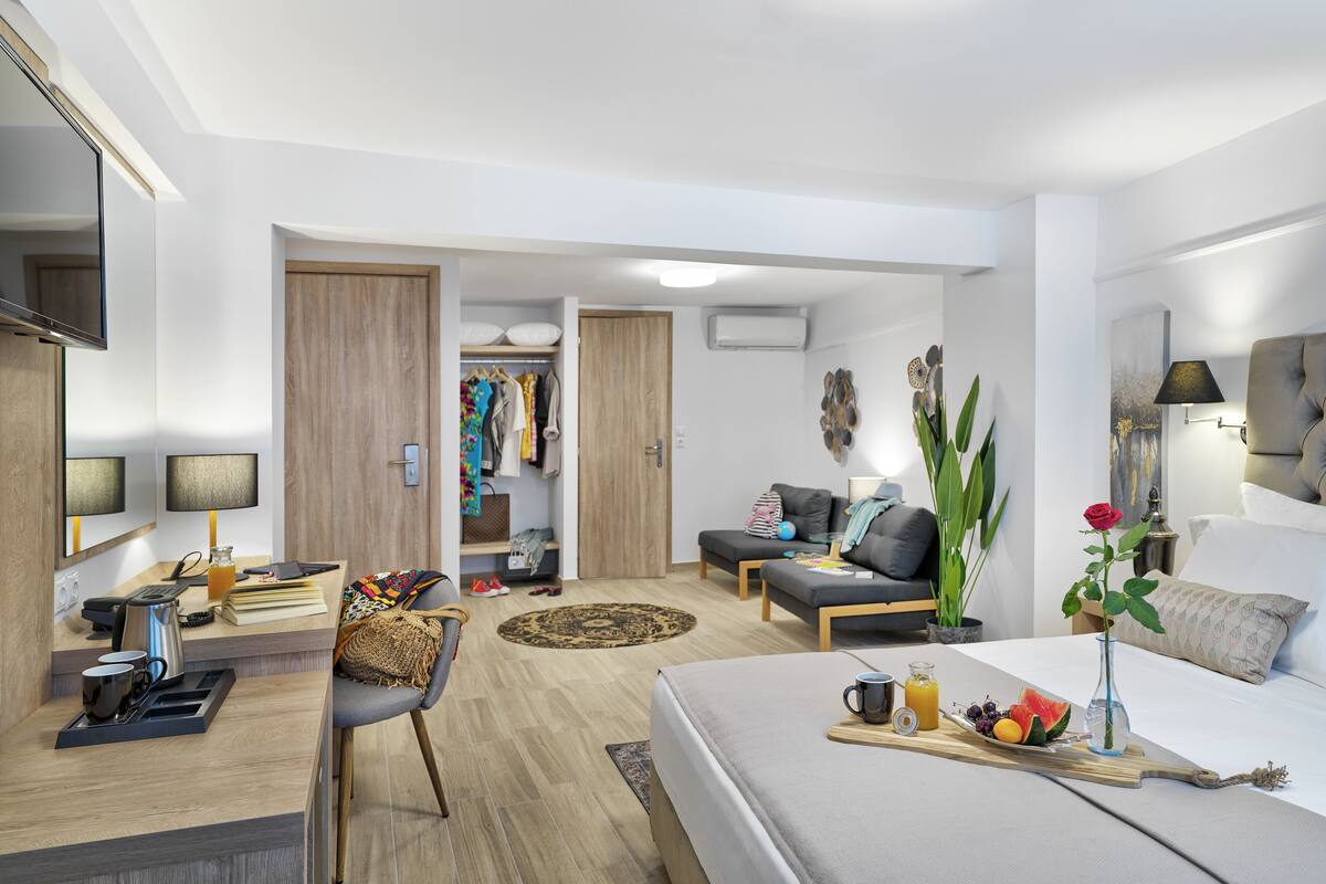 A modern hotel room with a bed, a sofa, a dining area, and a walk-in closet.