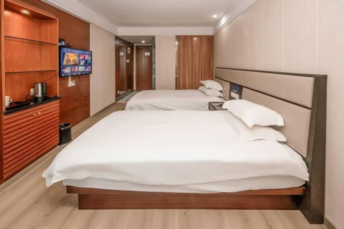 A hotel room with a large bed, a TV mounted on the wall, and a wooden cabinet.