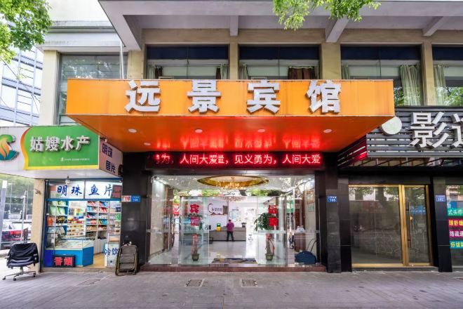 A hotel entrance with a prominent orange sign, glass doors, and a visible interior through the glass.