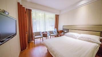 Habitación de hotel con una cama grande, televisión, escritorio, dos sillas y ventana con cortinas.