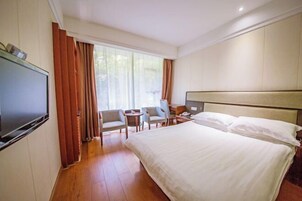 Habitación de hotel con una cama grande, televisión, escritorio, dos sillas y ventana con cortinas.