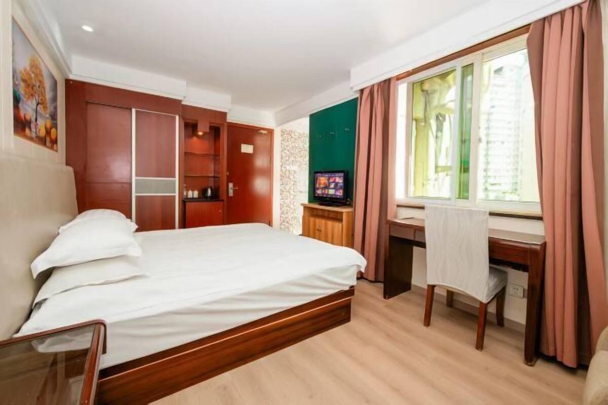 A hotel room with a bed, a desk, a chair, a television, and a window with curtains.