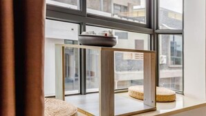 A modern room with a large window, a wooden table with a bowl, and a woven stool. - Haoxuan Inn (Wuyishan)