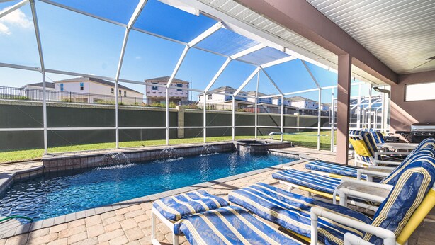 En pool med solstolar, ett överbyggt område och utsikt över hus i bakgrunden.