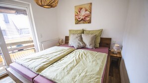 Ein Schlafzimmer mit Bett, Kissen, Nachttisch, Lampe, einem Gemälde und Blick durch ein Fenster.