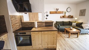 Eine kompakte Küche mit Backofen, Mikrowelle und einer Holzarbeitsplatte. Im Wohnbereich befindet sich ein grünes Sofa und ein kleiner Holztisch.