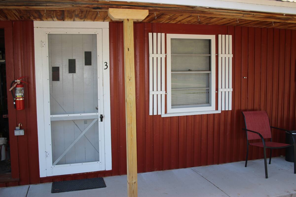 A red building with a white door marked with the number 3, a window with shutters, and a chair outside.