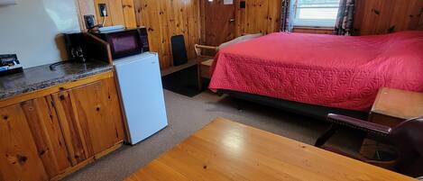 Une pièce avec un plafond en bois, un lit recouvert d’une couverture rouge, un bureau avec un ordinateur, une chaise et une table en bois.