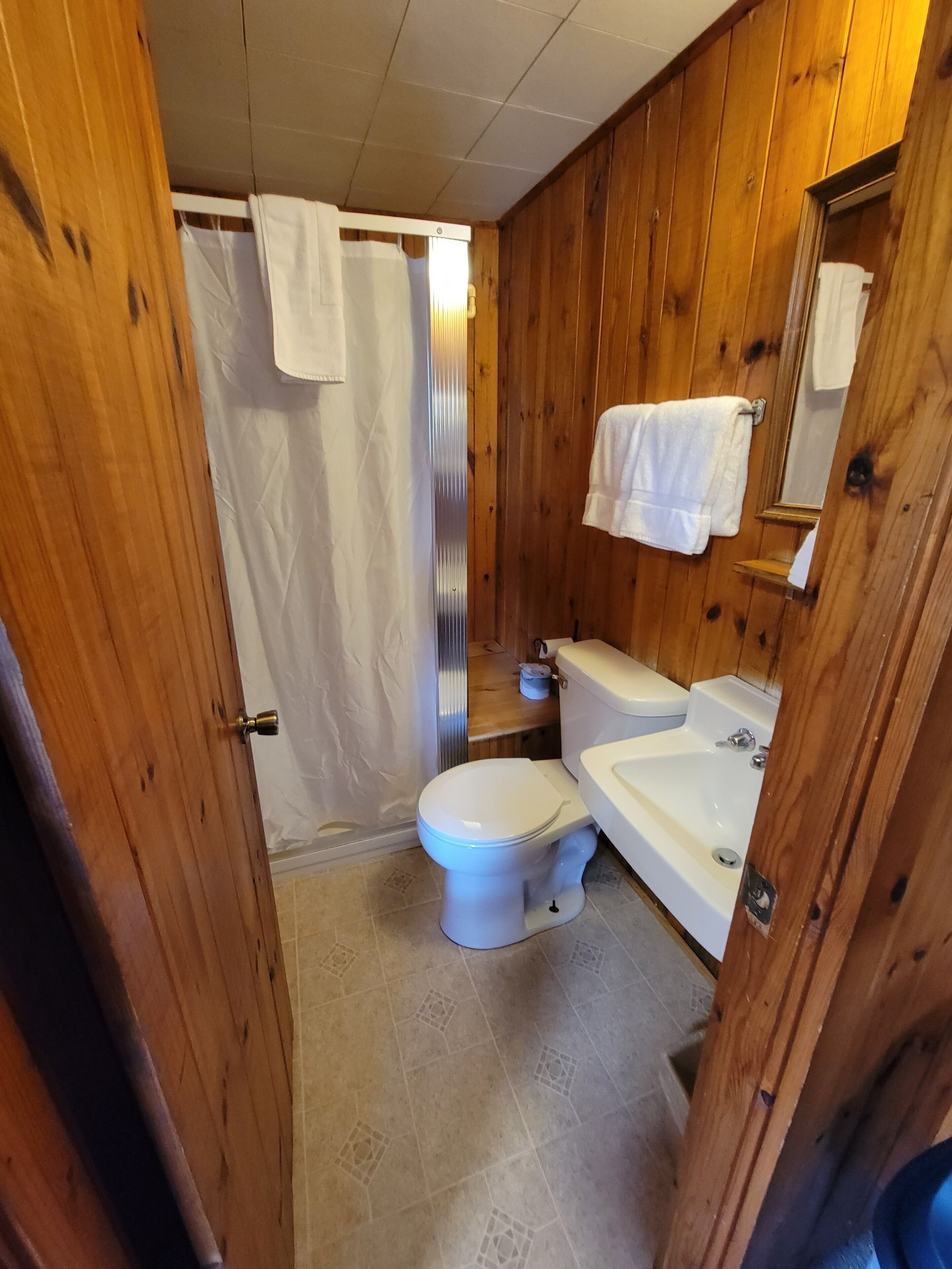 Un baño con paneles de madera, un inodoro, lavamanos y ducha.
