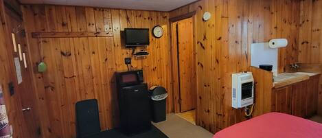 A room with wooden walls, two beds with pink bedding, a television, a microwave, a heater, and a trash bin.